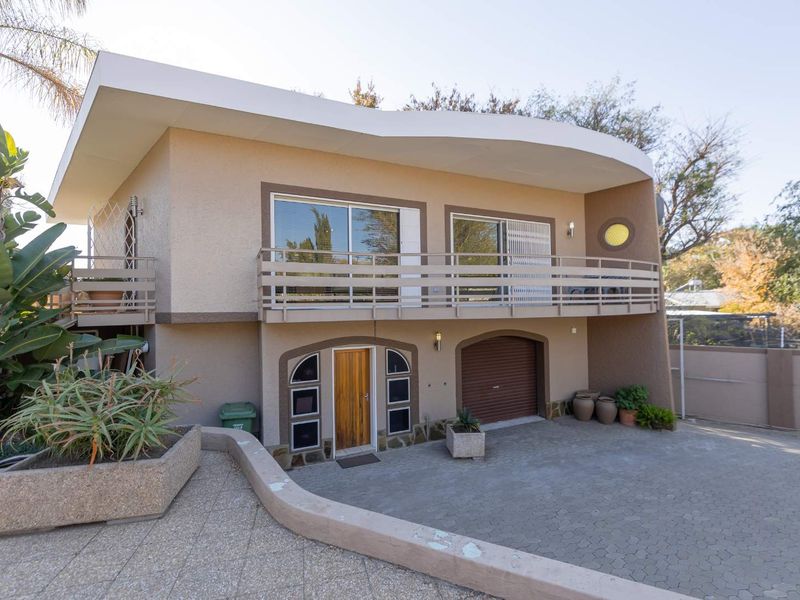 Front elevation of a two-story house featuring a balcony, integrated garage, and paved driveway with established landscaping.