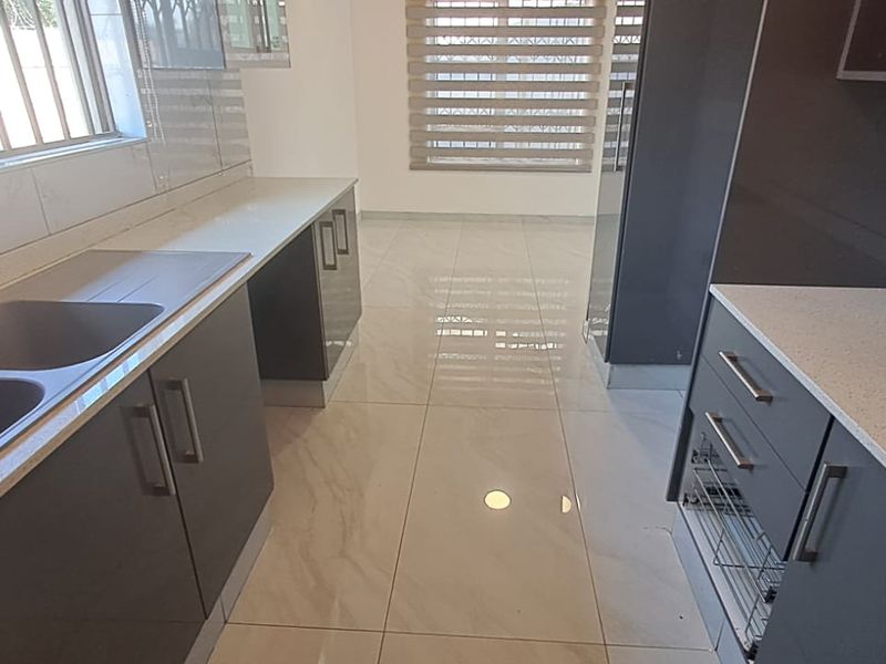 Modern kitchen featuring sleek grey cabinetry, quartz countertops, a double basin sink with a gooseneck tap, and polished tiled flooring.