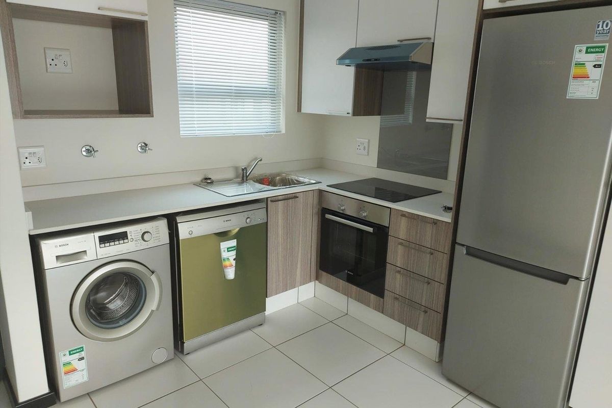 Modern kitchen featuring built-in cabinetry, laminate countertops, integrated oven, hob, and extractor fan, with tiled flooring and a window with venetian blinds.