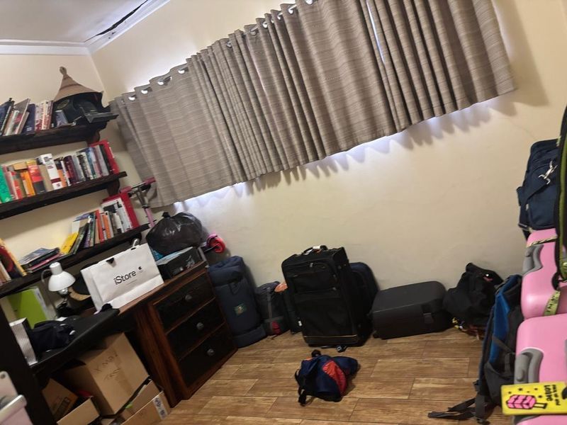 A bedroom featuring tiled flooring, built-in shelving, and curtain tracks, currently showing signs of wear including wall cracks and ceiling paint deterioration.