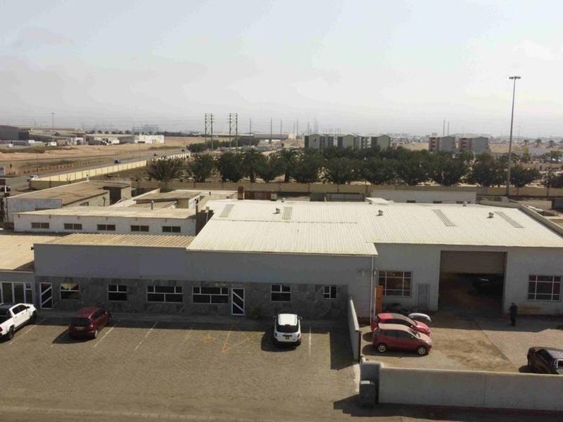 Aerial view of a commercial industrial property featuring a large warehouse structure with metal roofing, roller shutter access, and an adjacent paved parking lot.