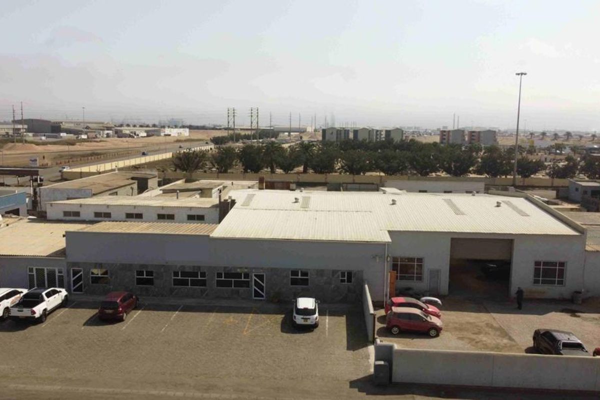 Aerial view of a commercial industrial property featuring a large warehouse structure with metal roofing, roller shutter access, and an adjacent paved parking lot.
