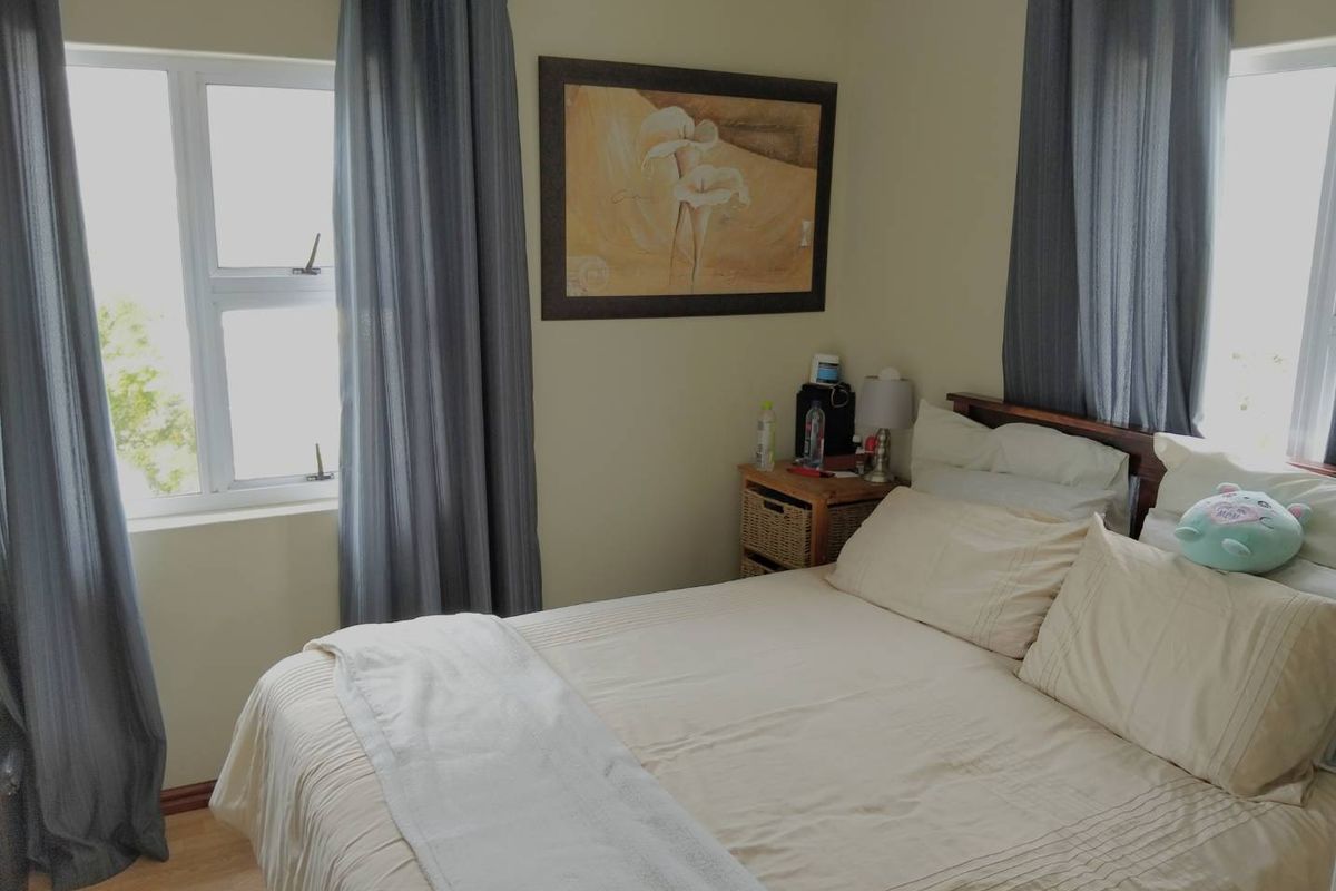 A functional bedroom featuring laminate flooring and dual windows with aluminium frames, providing natural light and a neutral backdrop.