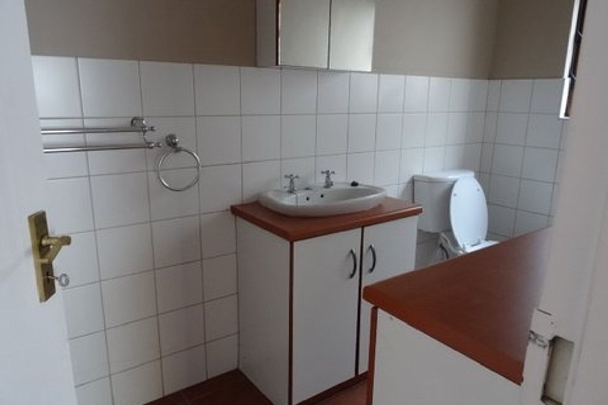 A functional bathroom featuring a vanity cabinet with a basin, a toilet, and wall-mounted towel rails with tiled splashbacks.