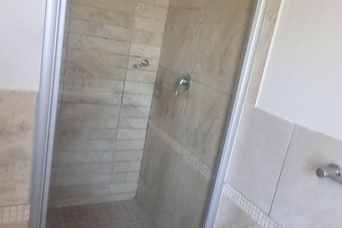 A clean, functional bathroom shower enclosure featuring neutral-toned wall and floor tiling with a glass door and chrome fixtures.