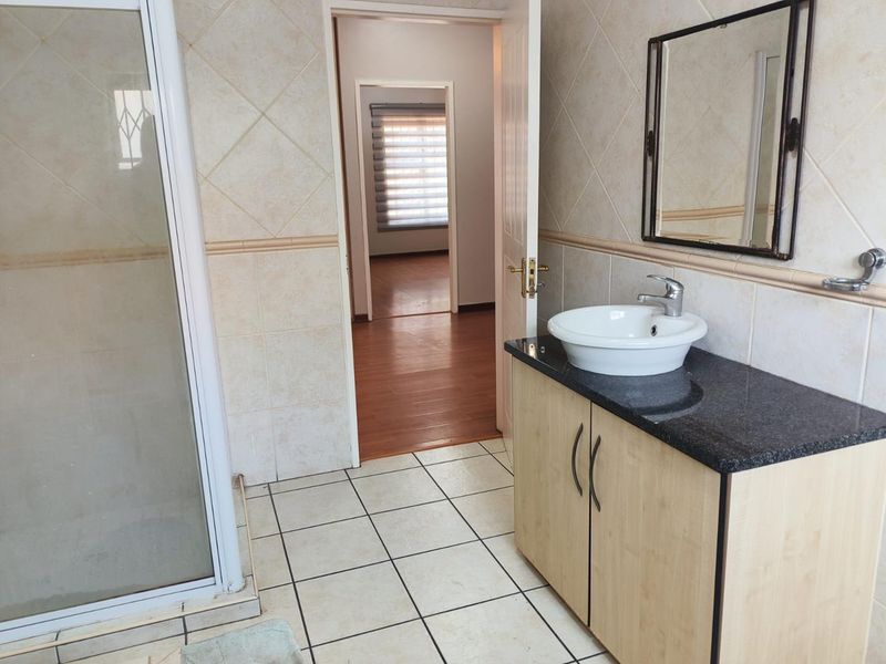 A functional bathroom featuring a shower enclosure, a vanity cabinet with a granite countertop, and a vessel sink, with tiled walls and flooring.