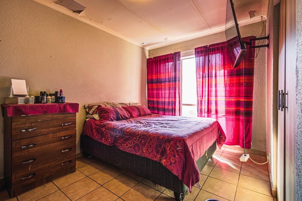 A bedroom featuring tiled flooring and a built-in wardrobe, currently showing significant signs of wear including damaged ceiling panels requiring repair.