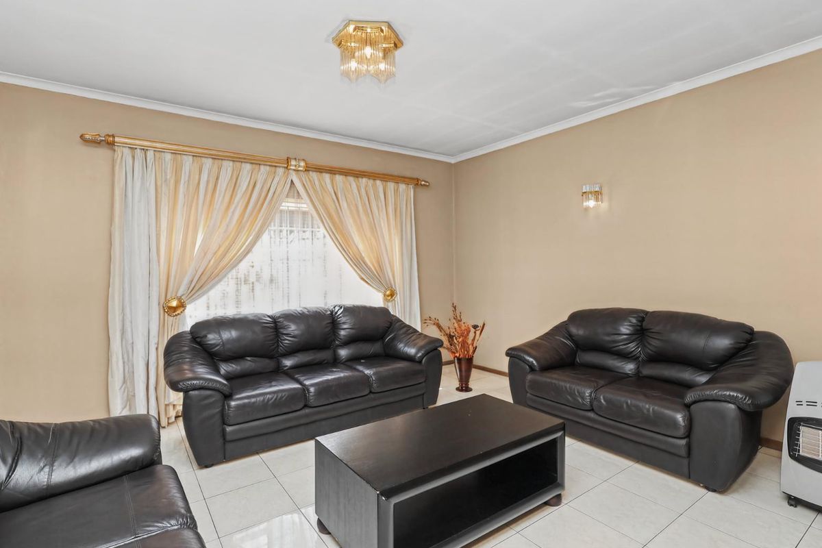 A spacious living room featuring neutral wall tones, tiled flooring, and classic ceiling and wall lighting fixtures.