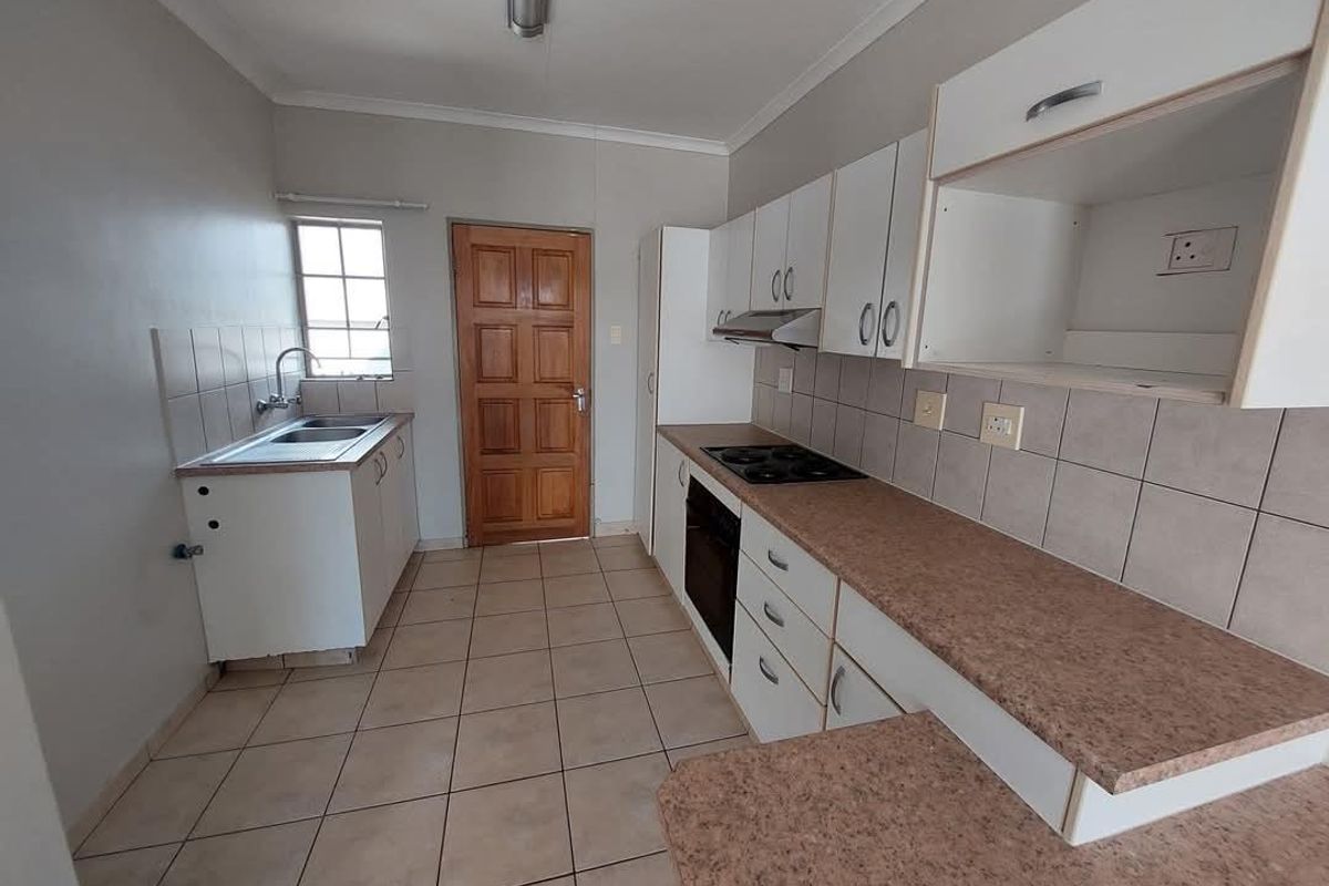 Functional kitchen featuring tiled flooring, laminate countertops, built-in oven and hob, extractor fan, and white cabinetry with direct access to an exterior door.