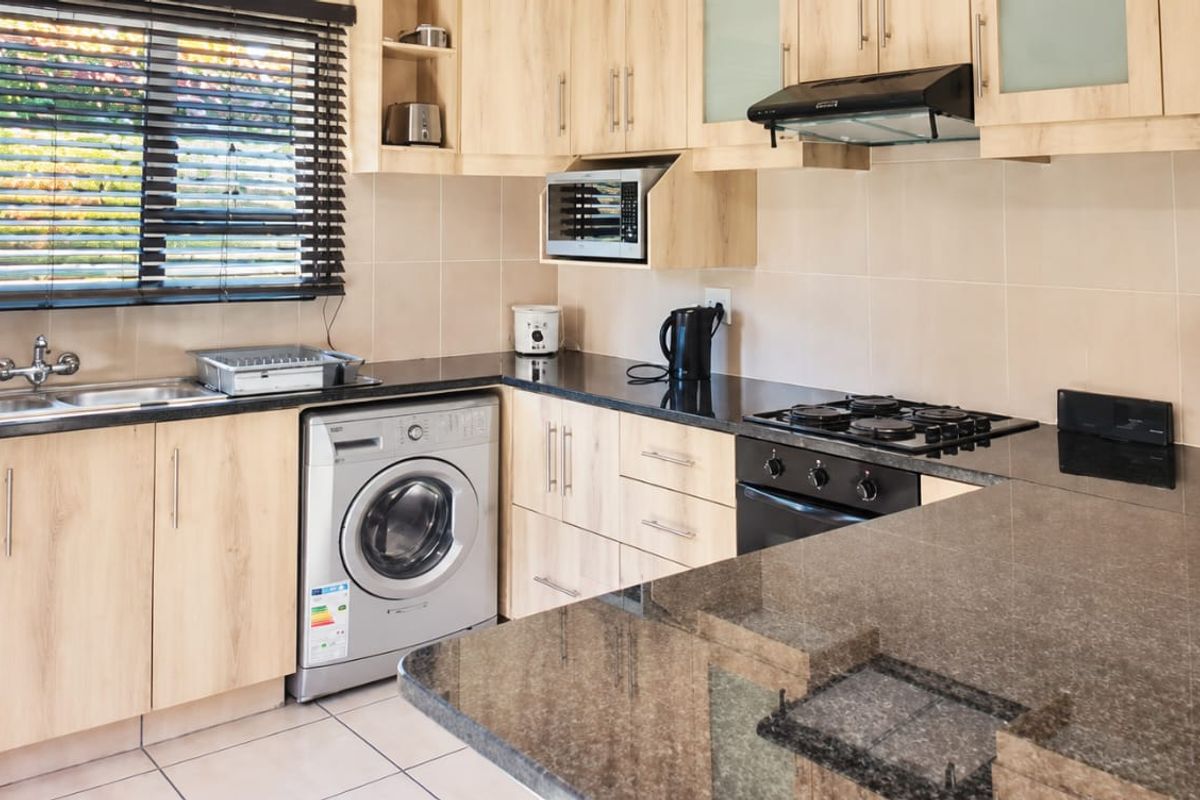 A functional kitchen featuring light wood cabinetry, dark granite countertops, a gas hob, built-in oven, and integrated microwave with tiled flooring and backsplash.