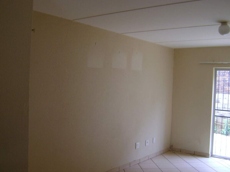 An empty living room featuring tiled flooring and a sliding glass door with a security gate, providing access to the exterior.