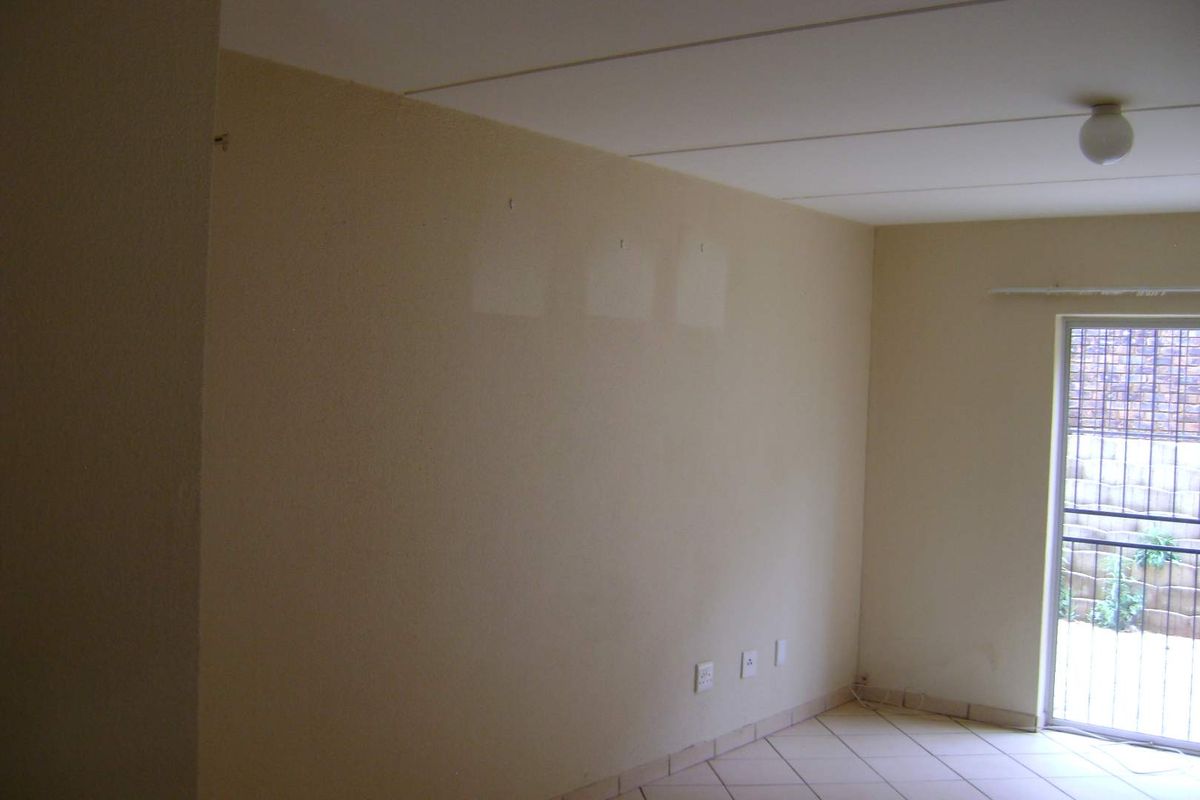 An empty living room featuring tiled flooring and a sliding glass door with a security gate, providing access to the exterior.