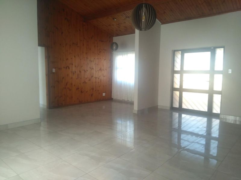Spacious living area featuring polished tiled floors, a striking timber-clad vaulted ceiling, and a large glass-paneled entrance door providing ample natural light.