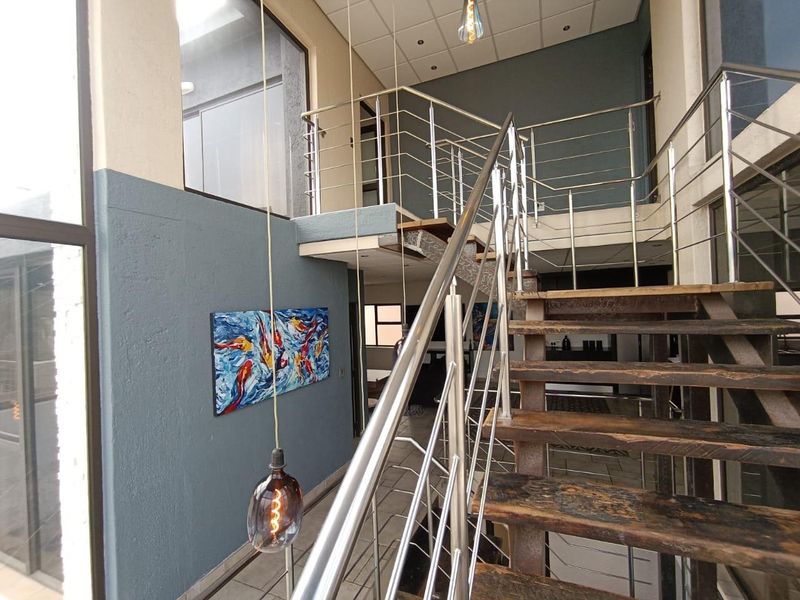 Modern double-volume hallway featuring a striking timber staircase with stainless steel balustrades, leading to an open mezzanine level with tiled flooring.