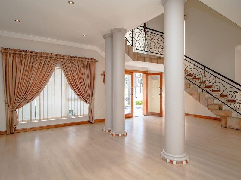 Spacious entrance hall featuring a grand staircase with wrought iron balustrades, decorative columns, and light laminate flooring.