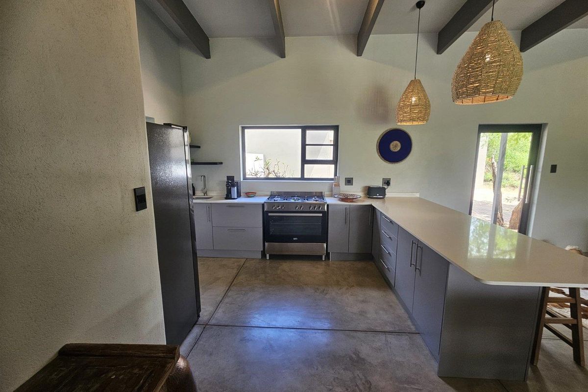 Modern kitchen featuring polished concrete floors, exposed ceiling beams, a large island with quartz countertops, and a gas stove.
