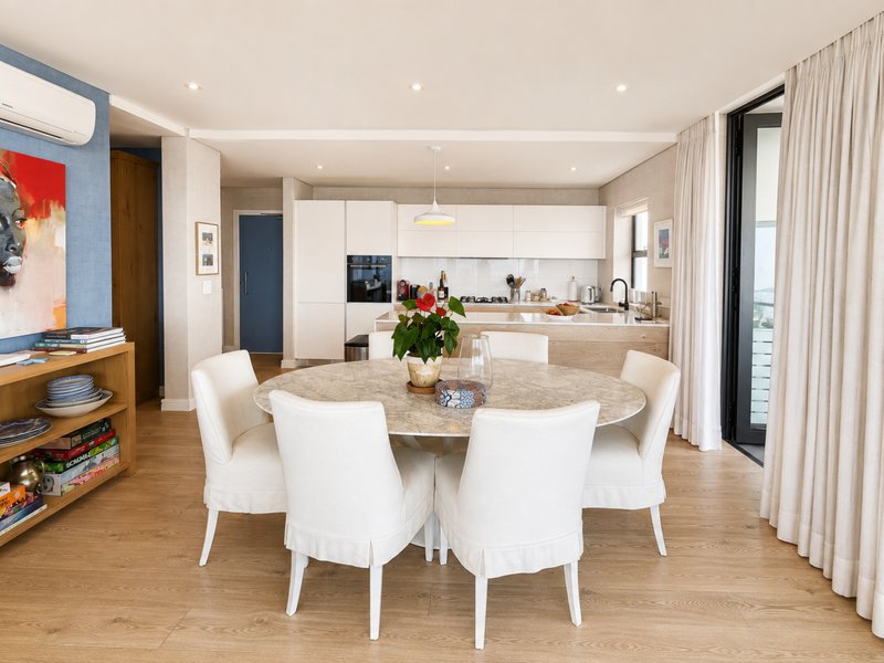Modern open-plan living and dining area featuring a sleek kitchen with integrated appliances, light wood-look flooring, and direct access to a balcony.