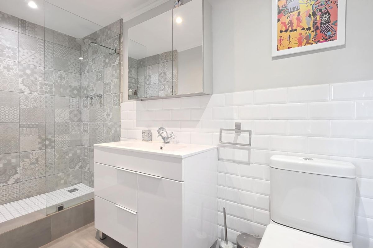 Modern bathroom featuring a walk-in shower with patterned feature tiles, a white vanity with basin, mirrored medicine cabinet, and classic subway wall tiling.