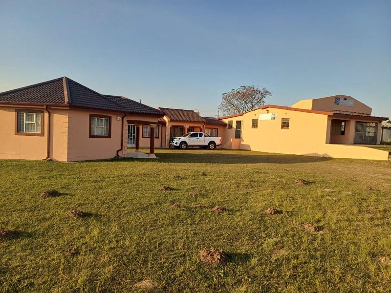 A wide-angle view of the property exterior featuring a large lawn, tiled roof structures, and a paved driveway area.