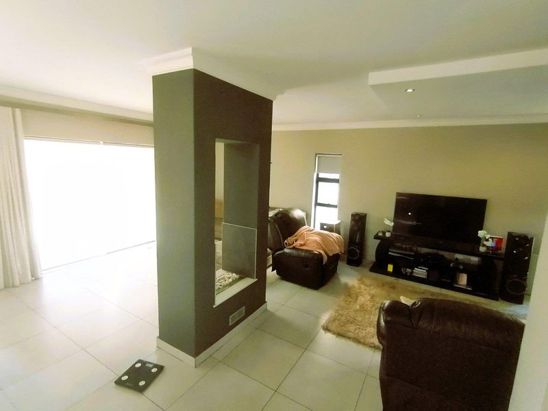 Spacious living area featuring tiled flooring, recessed ceiling lights, and a central built-in fireplace partition with access to outdoor space via sliding doors.