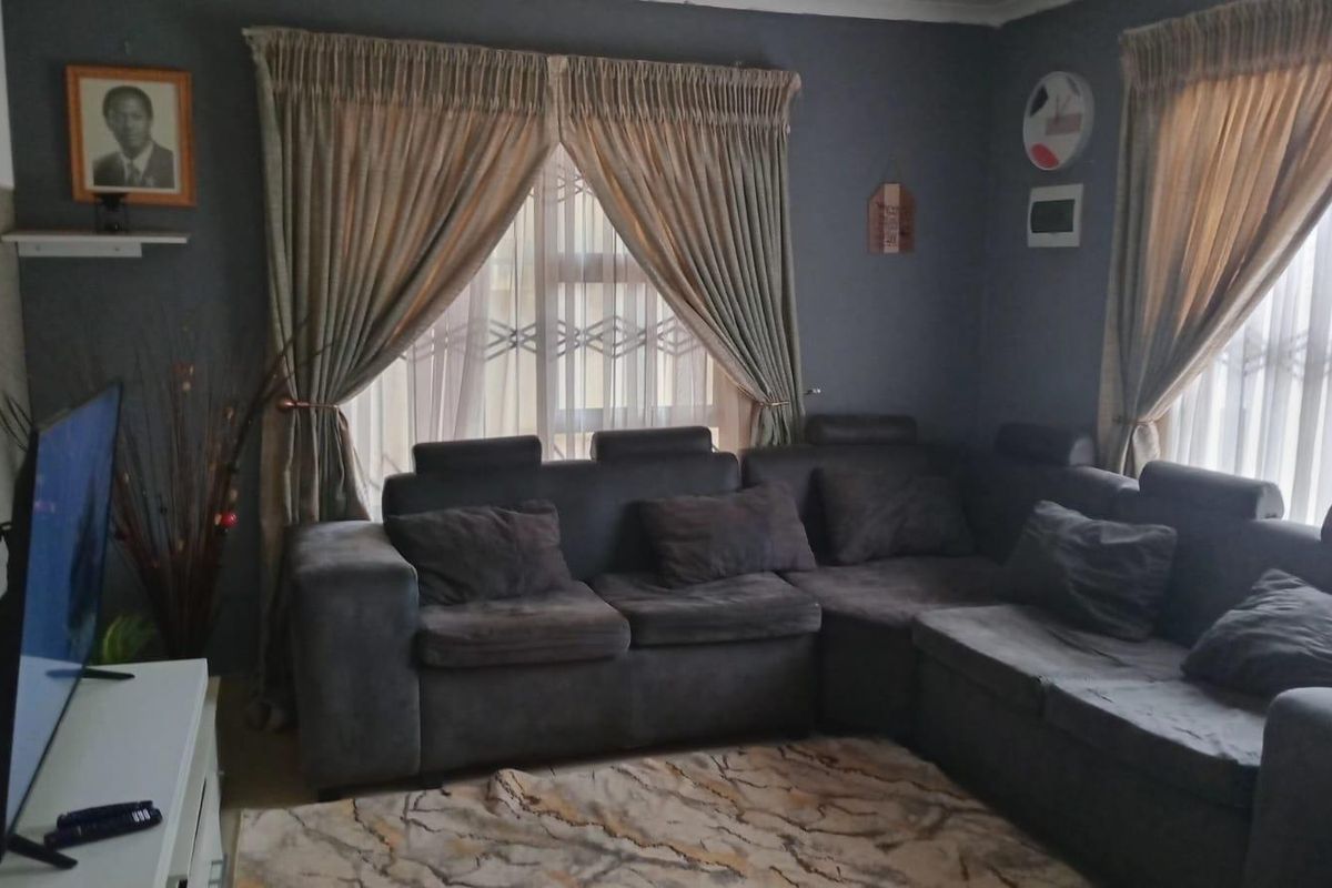 A cozy living room featuring dark grey walls, large windows with curtains, and security gates, providing a comfortable and private living space.