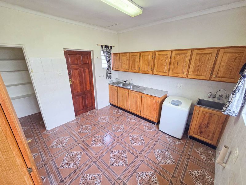A functional laundry room featuring built-in wooden cabinetry, a stainless steel sink, tiled flooring, and a separate walk-in pantry area.