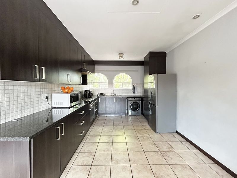 A functional kitchen featuring dark wood cabinetry, granite countertops, tiled backsplash, and integrated appliances, offering a clean and practical workspace.