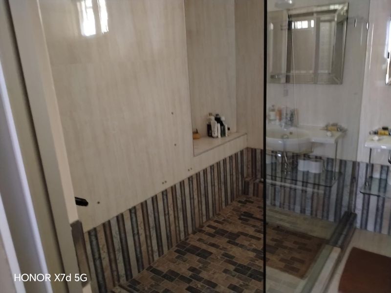 A bathroom featuring a glass shower enclosure, wall-mounted basin, and decorative tiled wall and floor finishes.