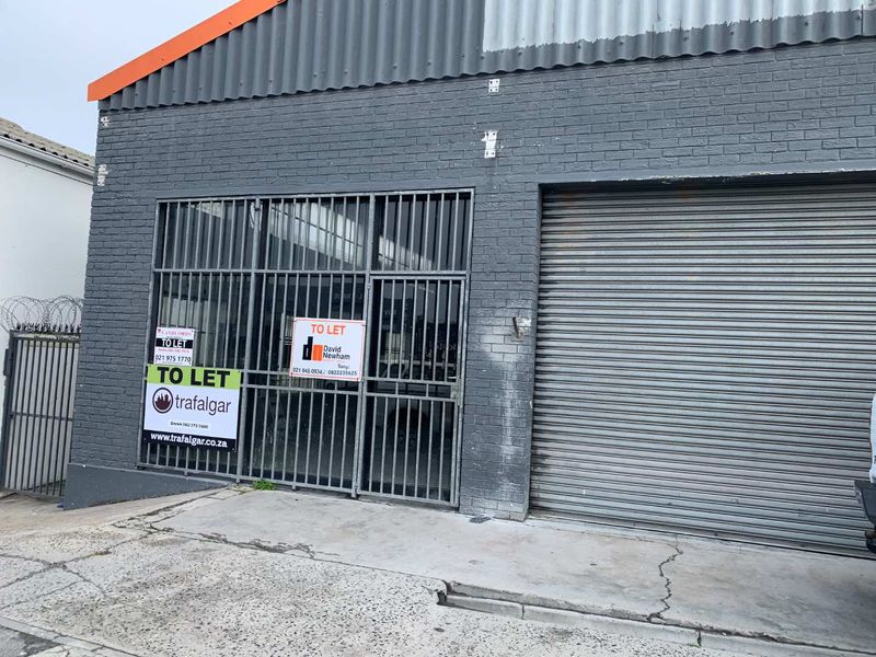 Front facade of a retail or industrial unit featuring a roller shutter door, security gate, and brick exterior with visible signage.