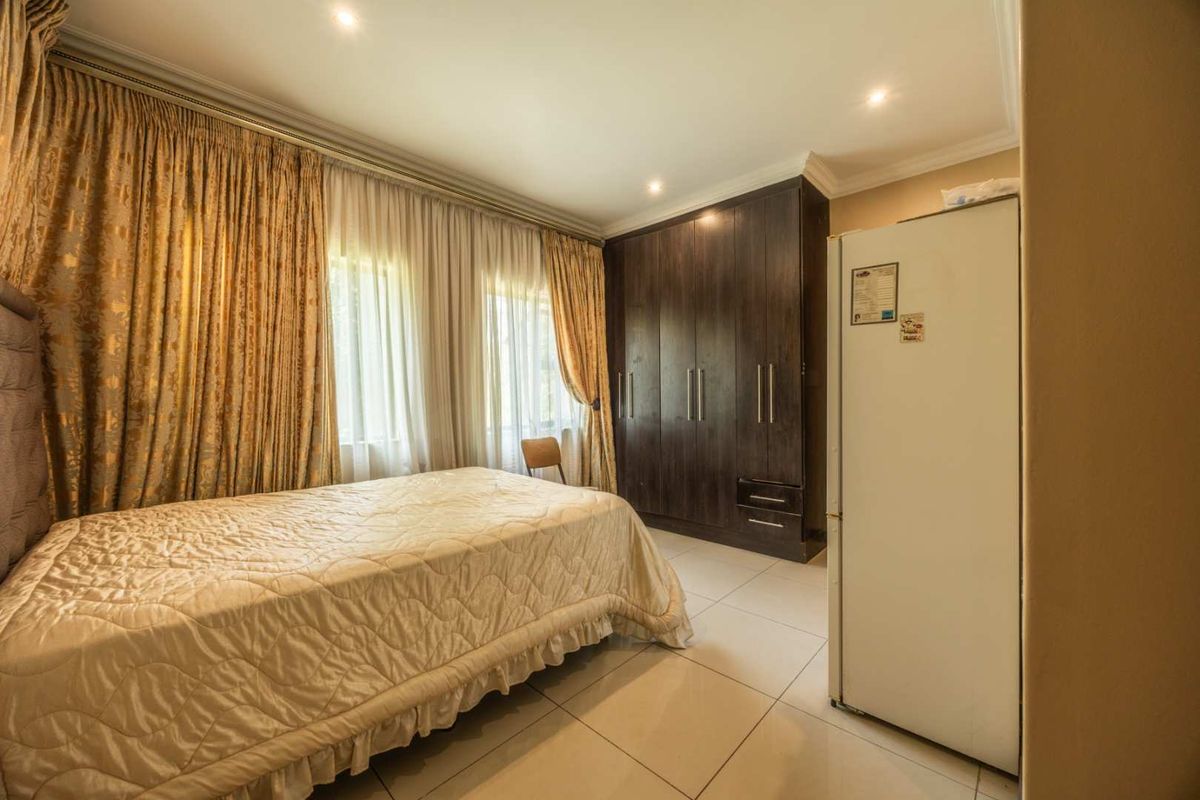 A well-maintained bedroom featuring built-in dark wood cupboards, tiled flooring, and recessed downlighting, offering a clean and functional living space.