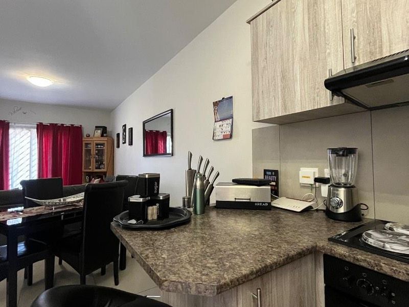 Open-plan kitchen and living area featuring light wood-look cabinetry, laminate countertops, and integrated cooking appliances, flowing into the adjacent dining space.