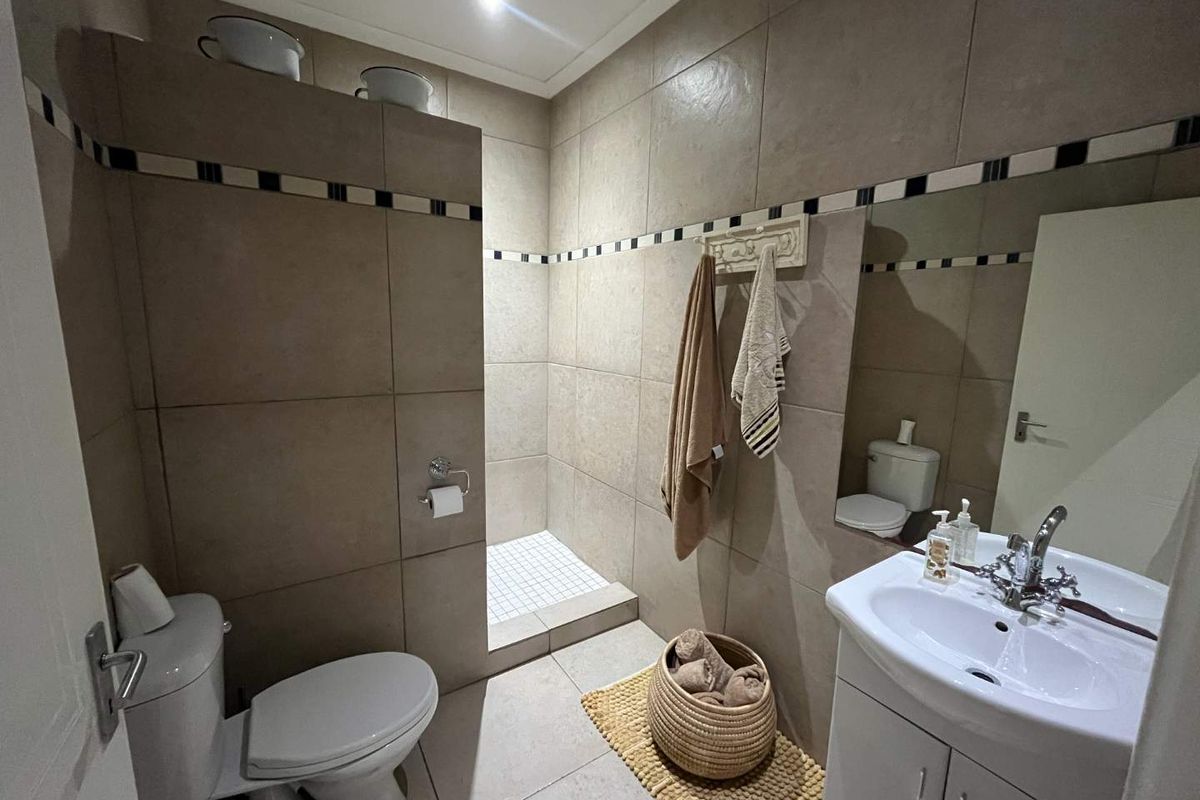 A functional bathroom featuring a walk-in shower with tiled walls, a vanity basin, and a toilet, finished with neutral ceramic floor and wall tiles.
