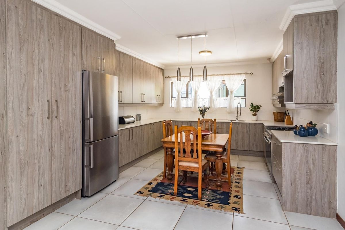 Spacious kitchen featuring modern wood-grain cabinetry, stone countertops, tiled flooring, and integrated cooking appliances, offering a functional and contemporary culinary space.