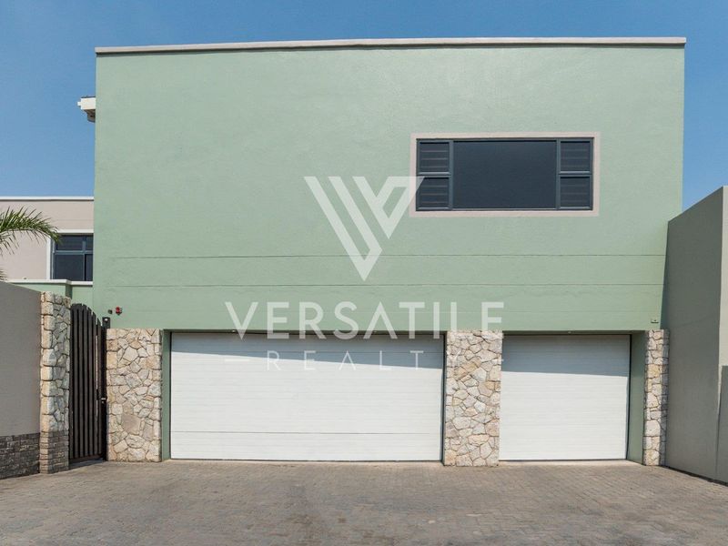Front elevation of the property featuring a double garage with stone cladding accents and a paved driveway.