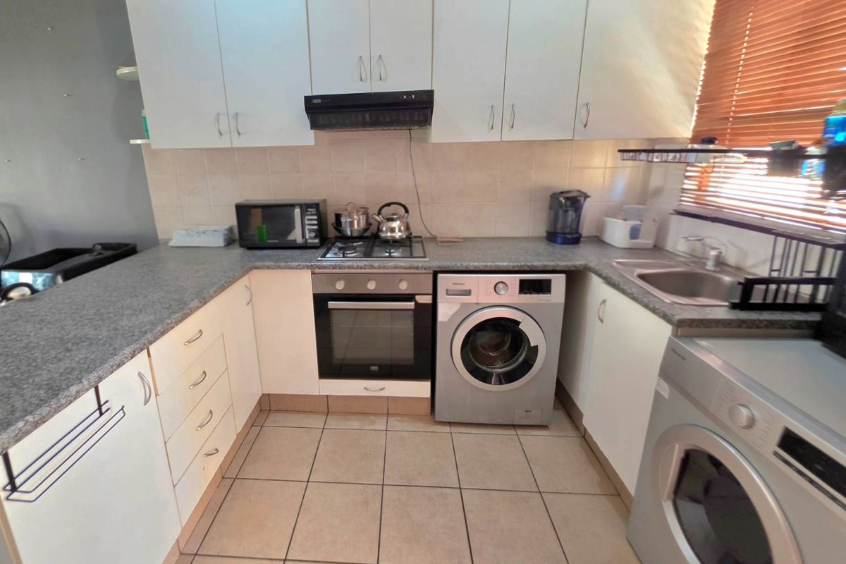 Functional kitchen featuring white cabinetry, granite-look countertops, built-in oven, hob, extractor fan, and integrated laundry appliance space.