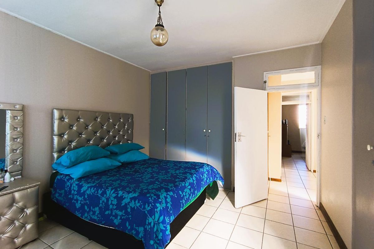 A bedroom featuring built-in cupboards, tiled flooring, and a pendant light fixture, with an open doorway leading to an adjacent hallway.