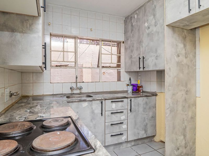 A compact kitchen featuring built-in cabinetry, laminate countertops, and an electric hob, currently requiring cosmetic updates and repairs to finishes.