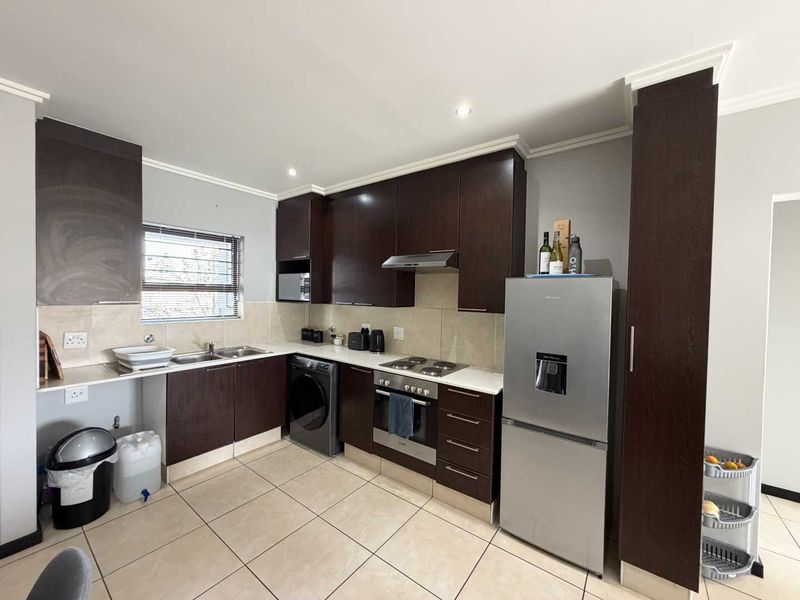 A functional kitchen featuring dark wood cabinetry, stainless steel appliances, tiled backsplash, and tiled flooring, offering a clean and practical workspace.