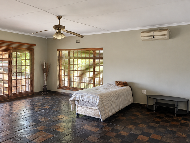 Spacious living area featuring slate tile flooring, a ceiling fan, split-system air conditioning, and large windows with wooden venetian blinds.