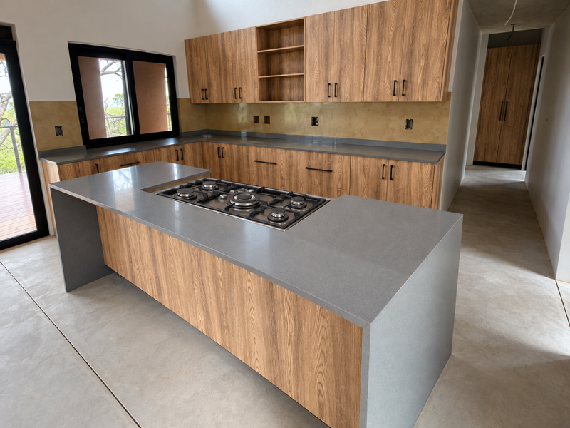 Modern kitchen featuring wood-grain cabinetry, stone countertops, a central island with a built-in gas cooktop, and polished concrete floors.