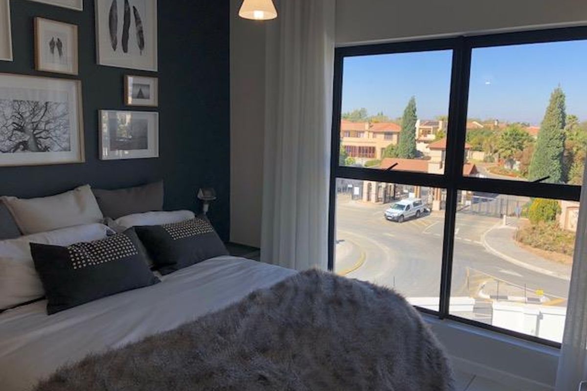 A well-maintained bedroom featuring a large window with views of the estate entrance, dark accent wall, and neutral tiled flooring.