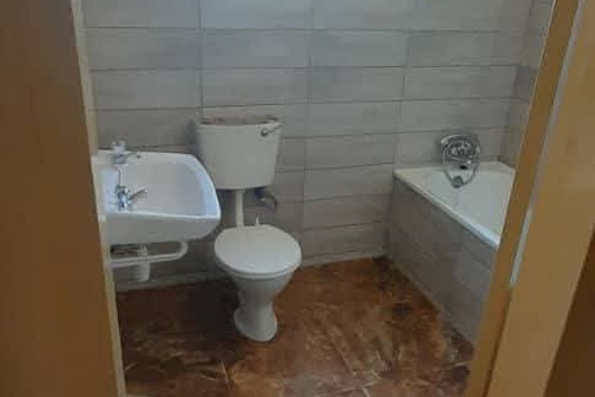 A functional bathroom featuring tiled walls and flooring, a standard bathtub, a wall-mounted basin, and a toilet.