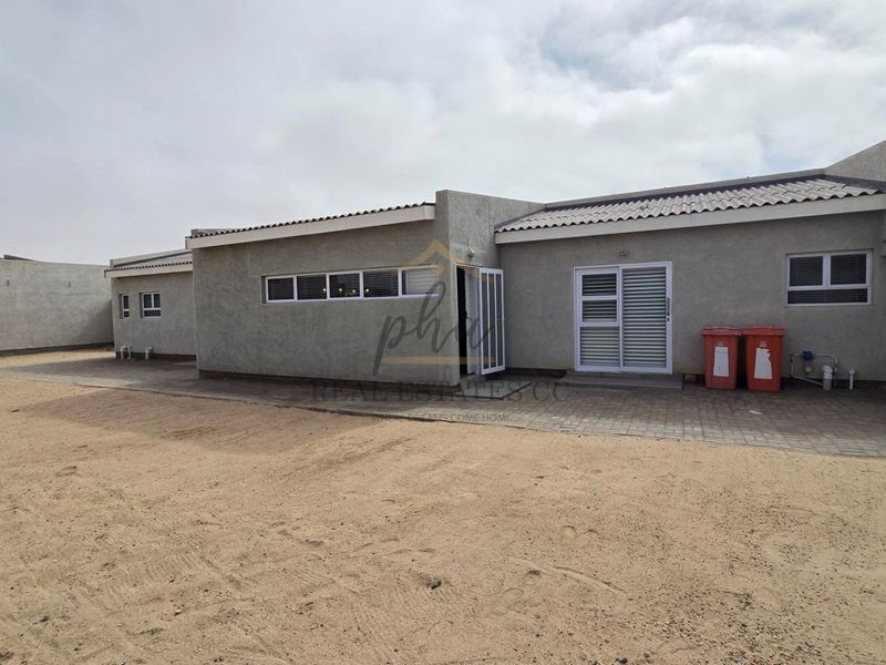 Rear view of the property featuring a paved patio area, sliding door access, and an expansive unlandscaped sandy yard.