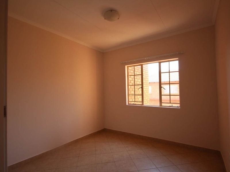 A clean, empty bedroom featuring neutral wall tones, tiled flooring, and a steel-framed window providing natural light.
