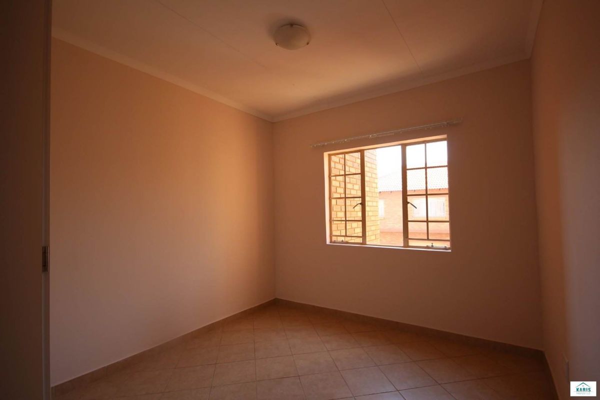 A clean, empty bedroom featuring neutral wall tones, tiled flooring, and a steel-framed window providing natural light.