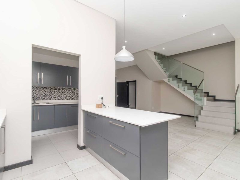 Modern open-plan living area featuring a sleek kitchen with grey cabinetry, a central island, and a contemporary staircase with a glass balustrade.