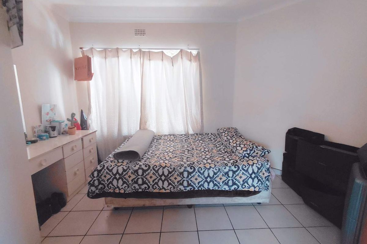 A bedroom featuring tiled flooring, a built-in vanity unit, and a window with curtain treatments.