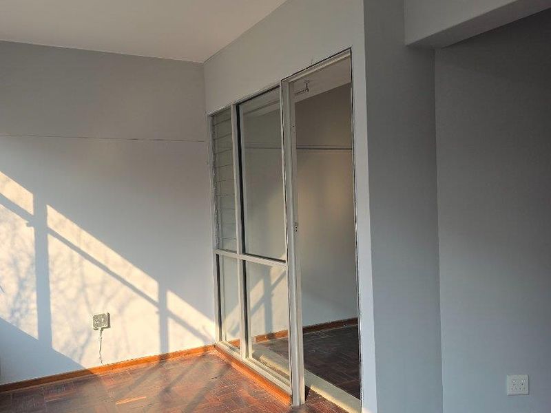An empty living area featuring classic parquet flooring, track lighting, and an aluminium sliding door leading to an adjacent space.
