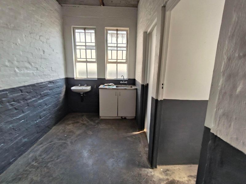 A functional utility space featuring exposed brick walls, concrete flooring, a built-in sink with cabinetry, and a separate wall-mounted basin.