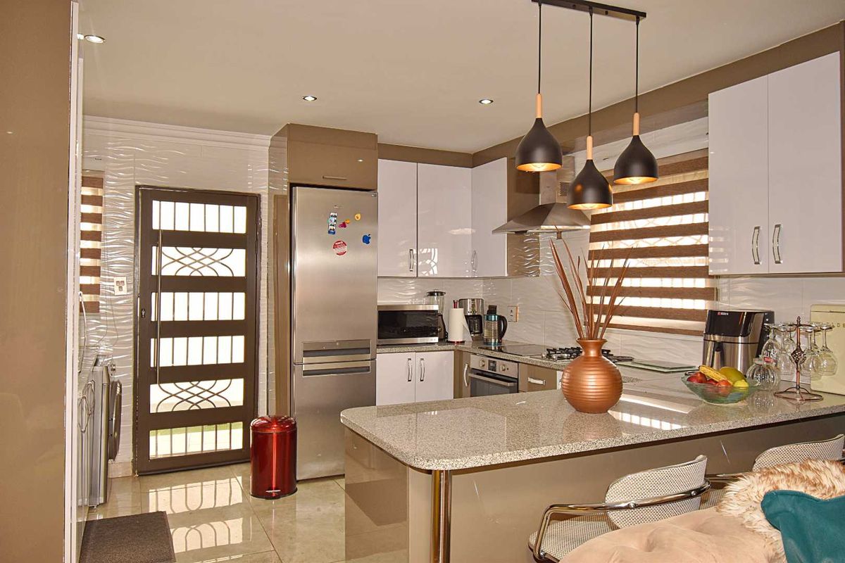 Modern kitchen featuring high-gloss cabinetry, granite countertops, a breakfast bar, built-in oven, and stainless steel extractor fan.